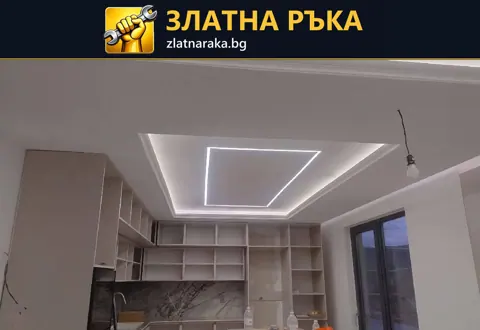 Окачен таван с осветен правоъгълник над незавършени кухненски шкафове и видими кабели