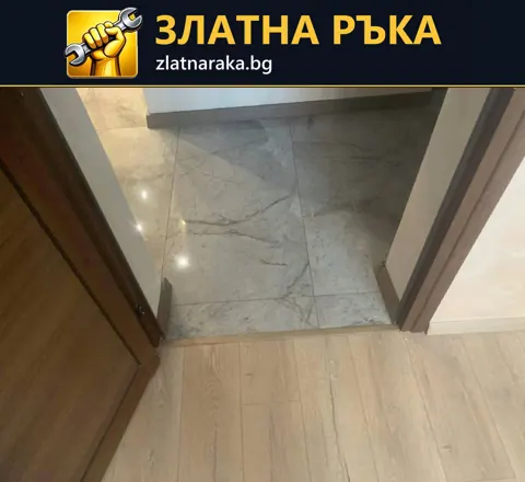 Праг между светла дървесна настилка и гланцирани сиви плочки под отворена кафява врата