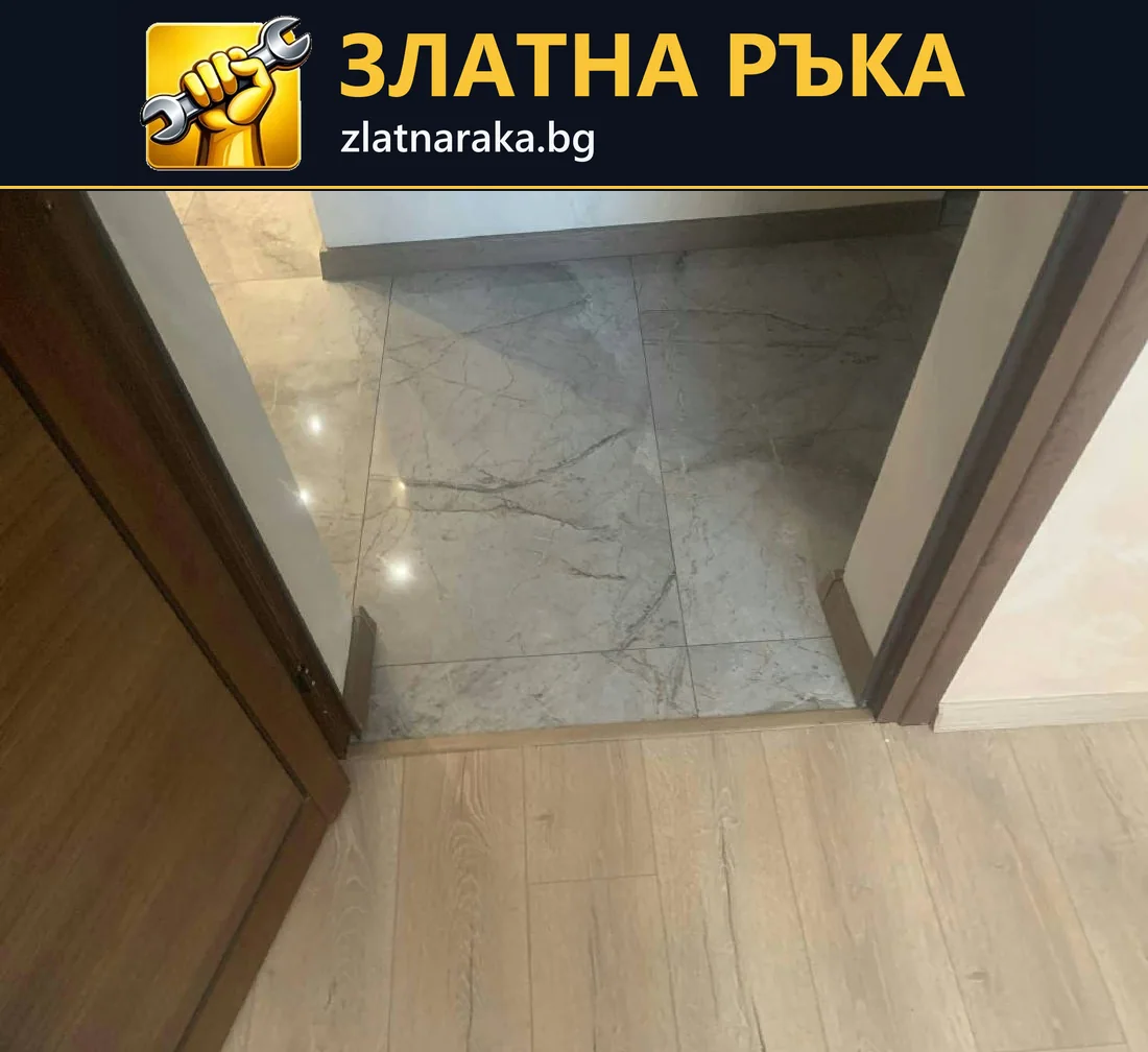 Праг между светла дървесна настилка и гланцирани сиви плочки под отворена кафява врата