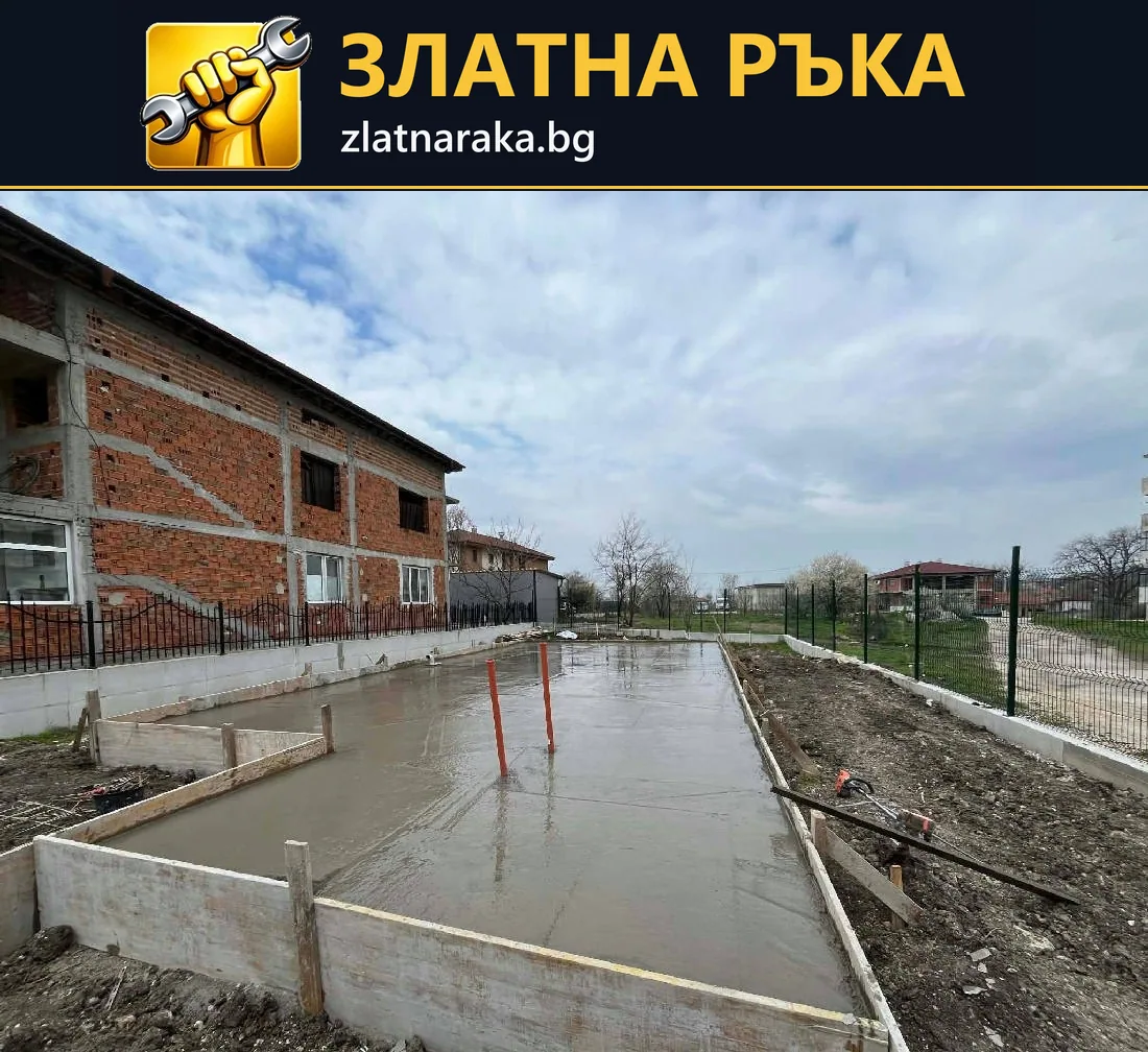 Дълга бетонна площ с дървен кофраж и изведени тръби се простира до тухлена сграда