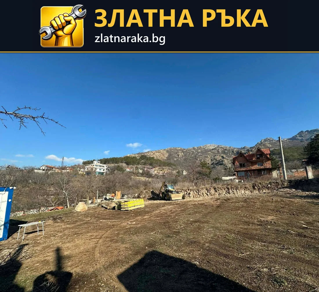 Подравнена земна площ с малка машина и материали в далечния край пред съседни къщи