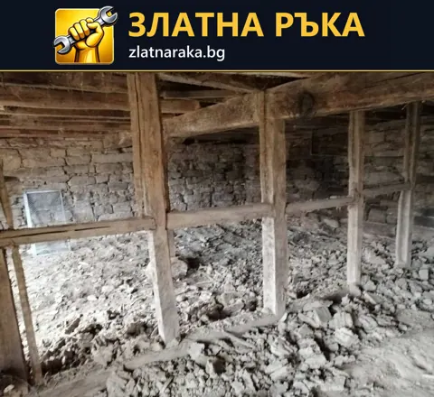 Старо помещение с открита дървена конструкция и натрупани строителни отломки.