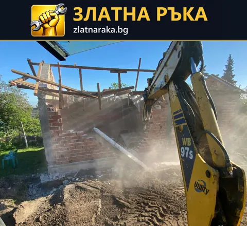 Багер разрушава тухлена стена на постройка с частично свален покрив.