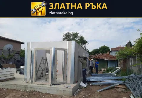 Сглобяване на малка постройка със светли стенни панели и метална рамка върху бетонна основа.