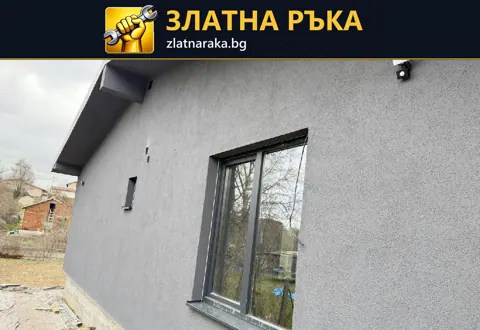 Сива завършена фасада с фина текстура, тъмна прозоречна дограма и покривна стреха.