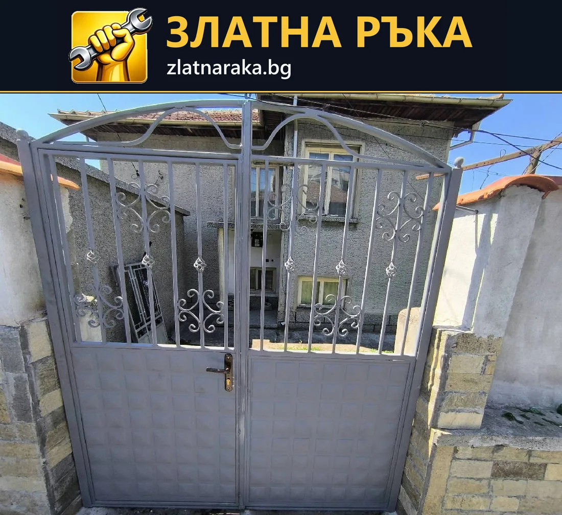 Двукрила сива порта с вертикални пръти, декоративни извивки и плътни долни панели между масивни стълбове