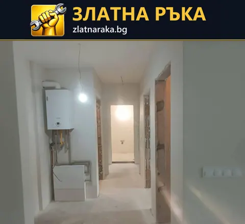 Дълъг бял коридор с отворени дверни отвори, висяща крушка и стенен уред с тръби отляво