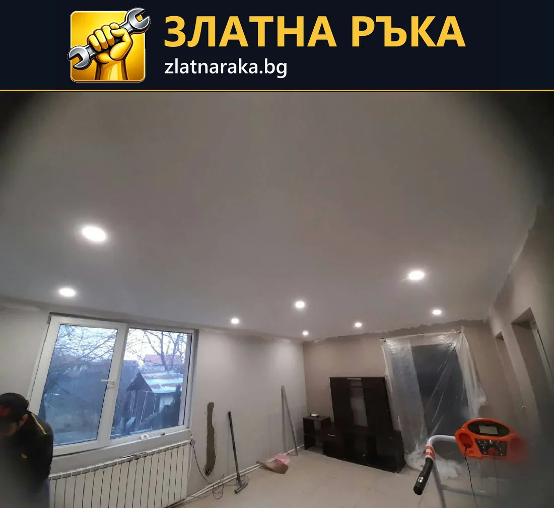 Гладък бял таван с множество малки вградени лампи над стая с прозорец и защитени мебели