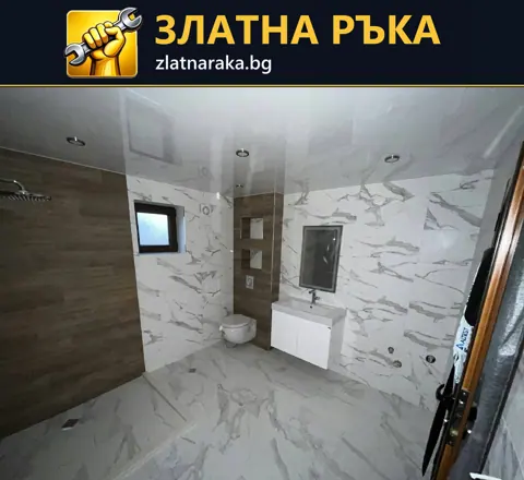 Светла баня с бели плочки с жилки, дървесна душова зона, бяла мивка и вградено осветление.