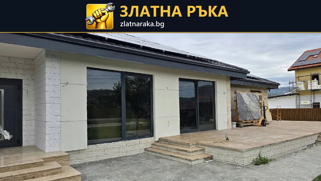 Фасада на ниска къща с широки тъмни прозорци, светла облицовка и стъпала
