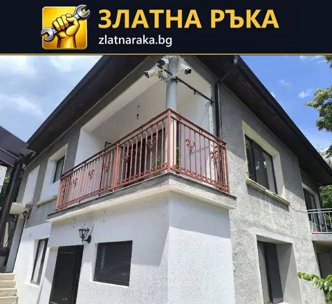 Двуетажна къща със светла фасада, тъмни кантове и червен метален парапет