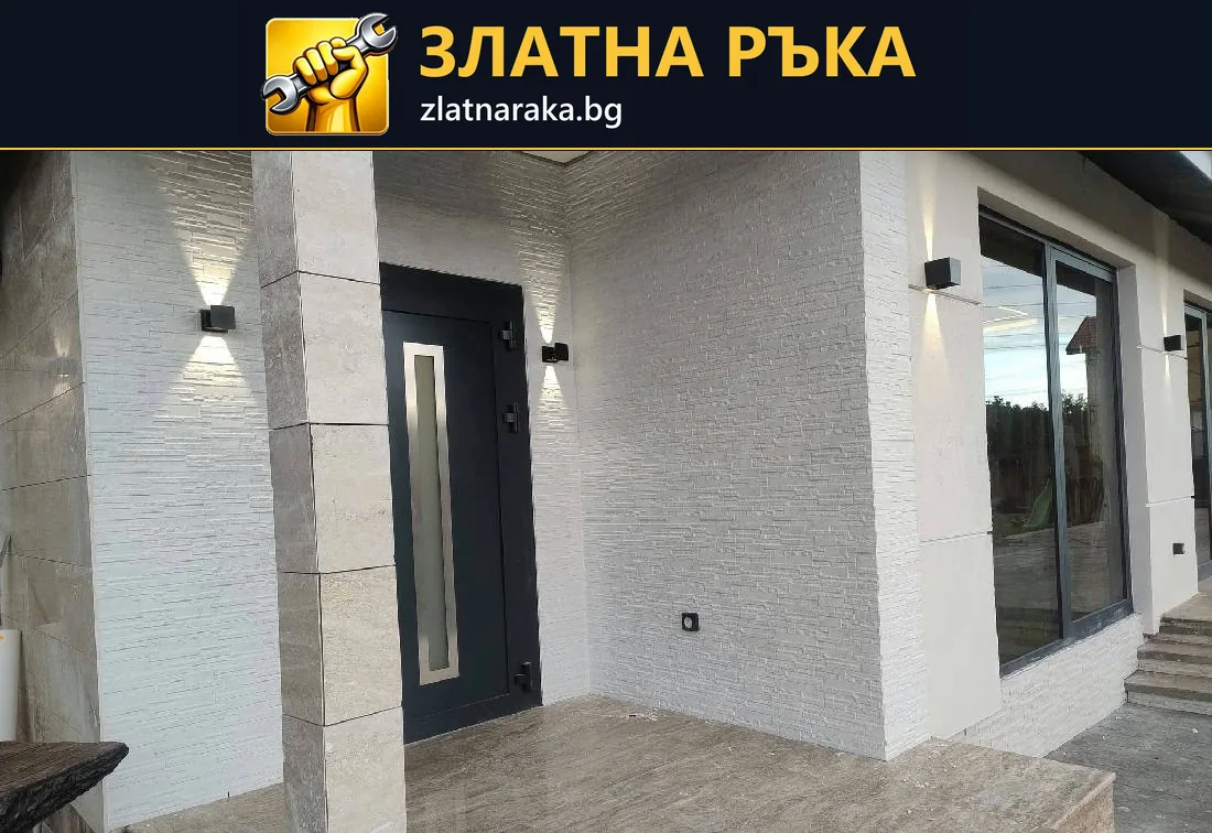 Вход с тъмна врата, светли релефни стени, облицована колона и стенни лампи.