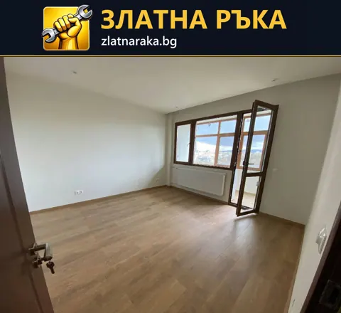 Празна стая със светли стени, дървесен под и кафява дограма с отворена балконска врата