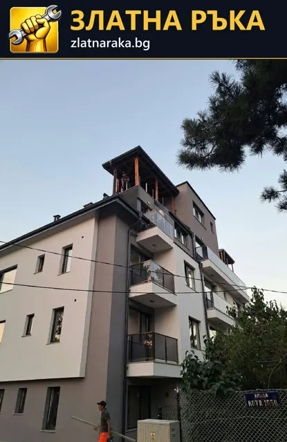 Многоетажна жилищна сграда със светла фасада, тъмни балконски парапети и по-високо оформен покривен обем