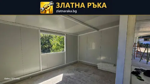 Вътрешност на сглобяемо помещение със светли стенни панели, открити профили и голям прозорец.