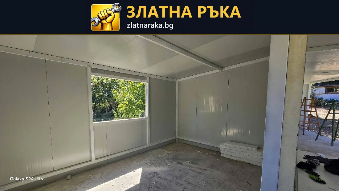Вътрешност на сглобяемо помещение със светли стенни панели, открити профили и голям прозорец.