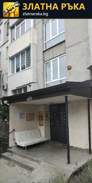 Тъмен метален навес над вход на жилищен блок с опорна колона пред вратата.