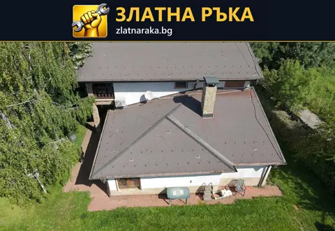 Завършен тъмен покрив с няколко ската и два комина сред зелен двор