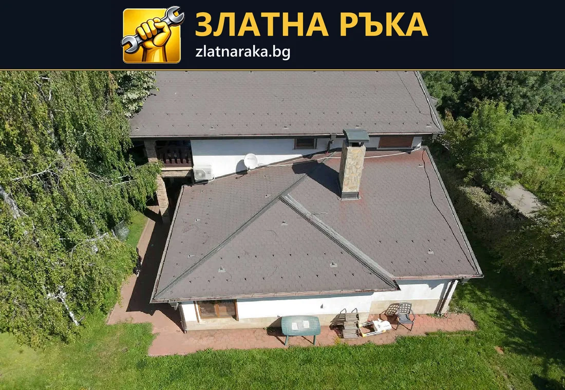 Завършен тъмен покрив с няколко ската и два комина сред зелен двор