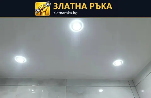 Гладък светъл таван с три кръгли светещи тела над облицовани стени