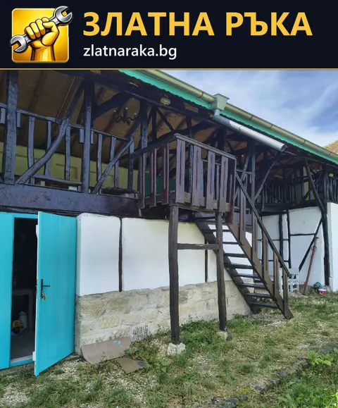 Тъмна права метална стълба с парапети и диагонални опори пред бяла фасада под дървен балкон