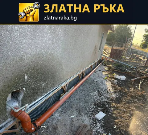Оранжева тръба с коляно и успоредни трасета в изкоп по цокъла на къща