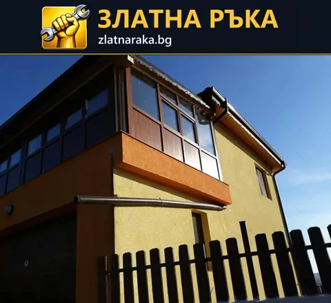 Двуетажна къща с жълта фасада, оранжев пояс и тъмно остъкляване на балкона.