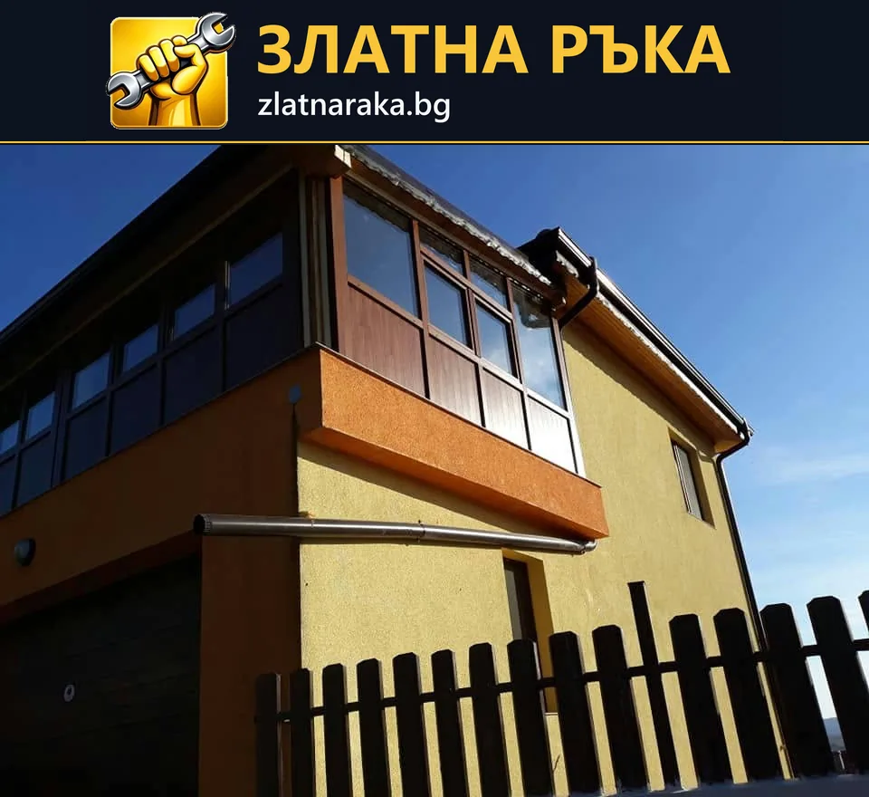 Двуетажна къща с жълта фасада, оранжев пояс и тъмно остъкляване на балкона.