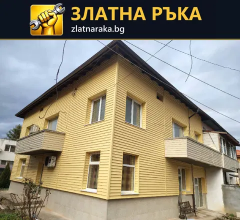 Жълта хоризонтална фасадна облицовка по двуетажна къща с два балкона и бели прозорци.